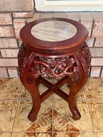 Front angle view of the round rosewood stand showing the carved floral and branch motifs along the apron and legs, and the marble inset top.