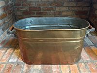 Front angled view of copper boiler log holder showing oval copper body and wood-handled side grips