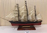 Full side view of the wooden Cutty Sark model ship showing all three masts with sails rigged and mounted on a wooden base.