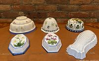 Front view showing six vintage ceramic jelly molds, including floral hexagonal, fish-shaped, dome and bell-shaped molds