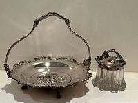 Photo showing the silver plated basket with ornate floral patterns and claw feet alongside the glass jam jar with silver plated floral lid.