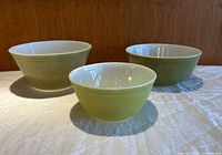 Photo of all three avocado green mixing bowls set on white cloth with wood panel background showing size range and shape.
