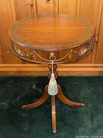 Front view of round walnut drum table with floral garland and brass hardware