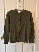 Front view of olive green knit cardigan with gold-tone buttons on hanger against a door.