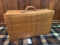 Full front view of tan woven leather suitcase with smooth leather trim and corner reinforcements