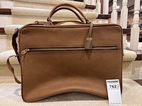 Front view of the brown vintage leather suitcase showing the padded handle and large zipper pocket on the front.