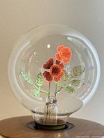 Clear glass vintage Aerolux style neon lightbulb with internal floral neon gas tubing design. Orange flower petals and green leaves inside the bulb are visible in the photos with the bulb illuminated.