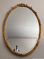 Front view of oval mirror showing entire gold gilt frame and reflective glass