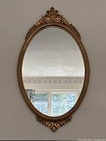 Full view of oval gilt wood frame and mirror surface hung on wall