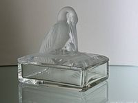 Side view of crystal dish with frosted pelican and frog lid figurines on reflective surface