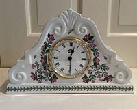Full view of the white porcelain mantel clock with floral decorations and ornate top design.