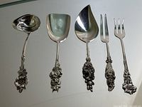Five floral handle utensils arranged side by side: small ladle, sugar scoop, sauce ladle and two forks.