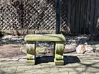 Front view of small stone bench on paved patio with lattice fence behind