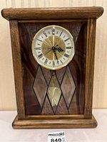 Front view of vintage oak mantle clock with stained glass diamond patterns and visible pendulum.