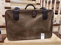 Front view of the taupe suede suitcase showing its leather handle, straps, and overall condition.