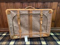 Front view of vintage suitcase showing tweed fabric, suede trim, buckled leather straps, zipper pocket, and handle.