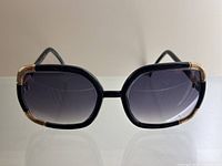 Front view of oversized black and gold sunglasses on reflective surface