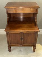 Front view of vintage walnut side table showing top surface, open middle shelf, and closed two-door cabinet with metal pull handles.