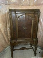 Front view of the antique wooden radio console with ornate carvings and double doors with brass-look handles.