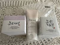 Photo shows three boxed Beauty of Joseon skin care products on a crocheted fabric surface: Revitalize Sleeping Mask, an unnamed tube cream, and Dynasty Anti-Wrinkle Face Cream boxed.