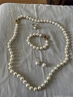 Full view of the faux pearl jewelry set including necklace, bracelet, earrings, and ring on fabric background.