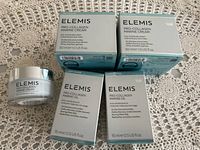 Five Elemis Pro-Collagen Marine skincare products arranged on a lace tablecloth. Two jars of marine cream and three boxes of marine oil.