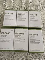 Six boxes of Elemis Superfood Facial Oil arranged on fabric surface, showing front packaging with branding and product details.
