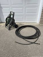 Photo showing two garden hoses, one green hose mounted on a gray Yardworks Hose Mobile winder and one longer black hose coiled on the ground.
