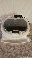 George Foreman Maxim grill with closed transparent lid, showing entire unit and power cord coiled on top.