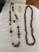 Full lot display showing the watch, Graziano tiger eye bead necklace with gold metal shapes and silver crystal balls, matching tiger eye ring, and brown coral-like necklace.
