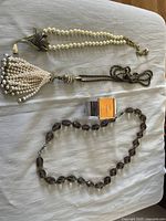 Full view of all four items including the pearl necklace with floral design and tassel necklace, the Joan Rivers watch and the brown beaded necklace.