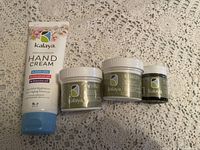 Four skincare products by Kalaya including one hand cream tube and three small jars on a crocheted lace tablecloth.