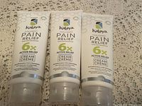 Three tubes of Kalaya Pain Relief cream on a lace surface, showing front labels.