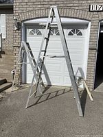 Three aluminum ladders placed in front of a garage door: a 6-step Lite Metals Model 506 with paint marks, a taller 9-step ladder of unknown brand with similar wear, and a smaller Ekco step ladder.