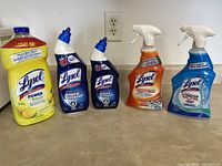 Full lot of five Lysol cleaning bottles and sprays shown on a counter including surface cleaner, toilet bowl cleaners, degreaser, and peroxide spray.