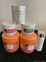 Group photo of all six M. Asam bath and body products including Vitamin E Cleansing Cream, Mandarine Grapefruit Peeling, Lemongrass Peeling, two jars of Happy Orange Body Butter, and Hydro Lotion Serum.