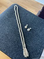 Full view of the imitation pearl lariat necklace laid on a dark surface with the pair of floral motif earrings beside it.