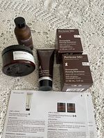 Five Perricone MD skincare products arranged on a lace background: jar moisturizer, tube cream, brown bottle, and two boxed moisturizers.