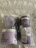 Three jars of Prai Ageless Throat and Decolletage Creme in purple containers with silver lids, two paired with purple polka dot eye masks, all new in clear plastic packaging.