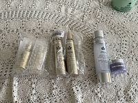 Full lot showing six Prai skin care products arranged on lace tablecloth: two bubble wrapped 24K Gold Precious Oil Drops, two gold retinol tubes, one large clear bottle with silver cap, and one small lavender jar.