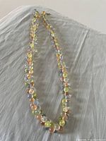 Full view of pastel multicolor glass bead necklace laid out on a white fabric background.