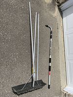 Full view of roof rake shovel head, metal handle, and two extension poles laid on pavement.