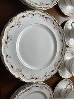 Close-up of a dinner plate showing white bone china with scalloped edges and gold and burgundy decorative border.