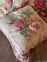 Close-up of square decorative pillow with raised pink flowers, green leaves, pink lace trim, dusty rose backing visible beneath