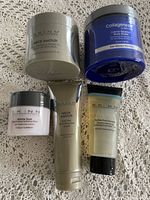 All 5 Skinn skincare products arranged on fabric, showing jars and tubes clearly.
