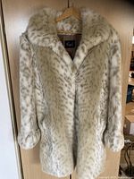 Full front view of mid-length snow leopard patterned faux fur coat on hanger, hanging on door.