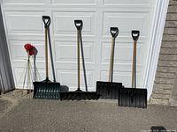 All four snow shovels lined up in front of garage door with ten red round reflectors clustered to the left