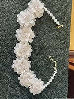 Full view of pink floral statement necklace with large pink flowers and pink bead chain on dark background