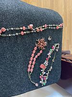 Photo showing three statement necklaces laid out on a dark fabric background, featuring various pink and multicolor beads, floral cloisonné beads, and starburst pendant with rhinestones.