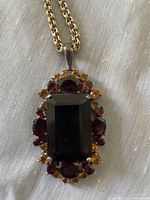 Close-up of gold tone chain necklace with large dark amber glass pendant surrounded by red and amber crystals
